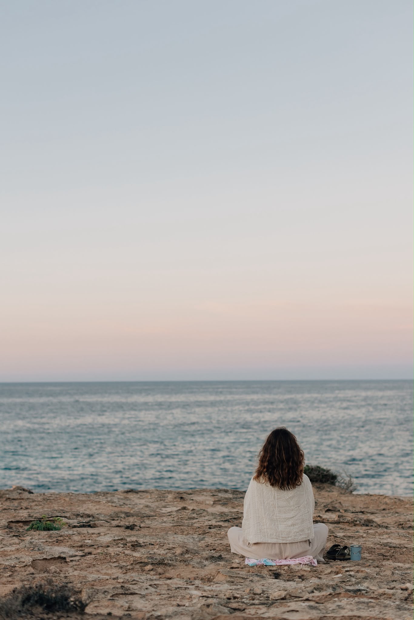 A woman sitting on the cliffs, looking out to sea at dusk